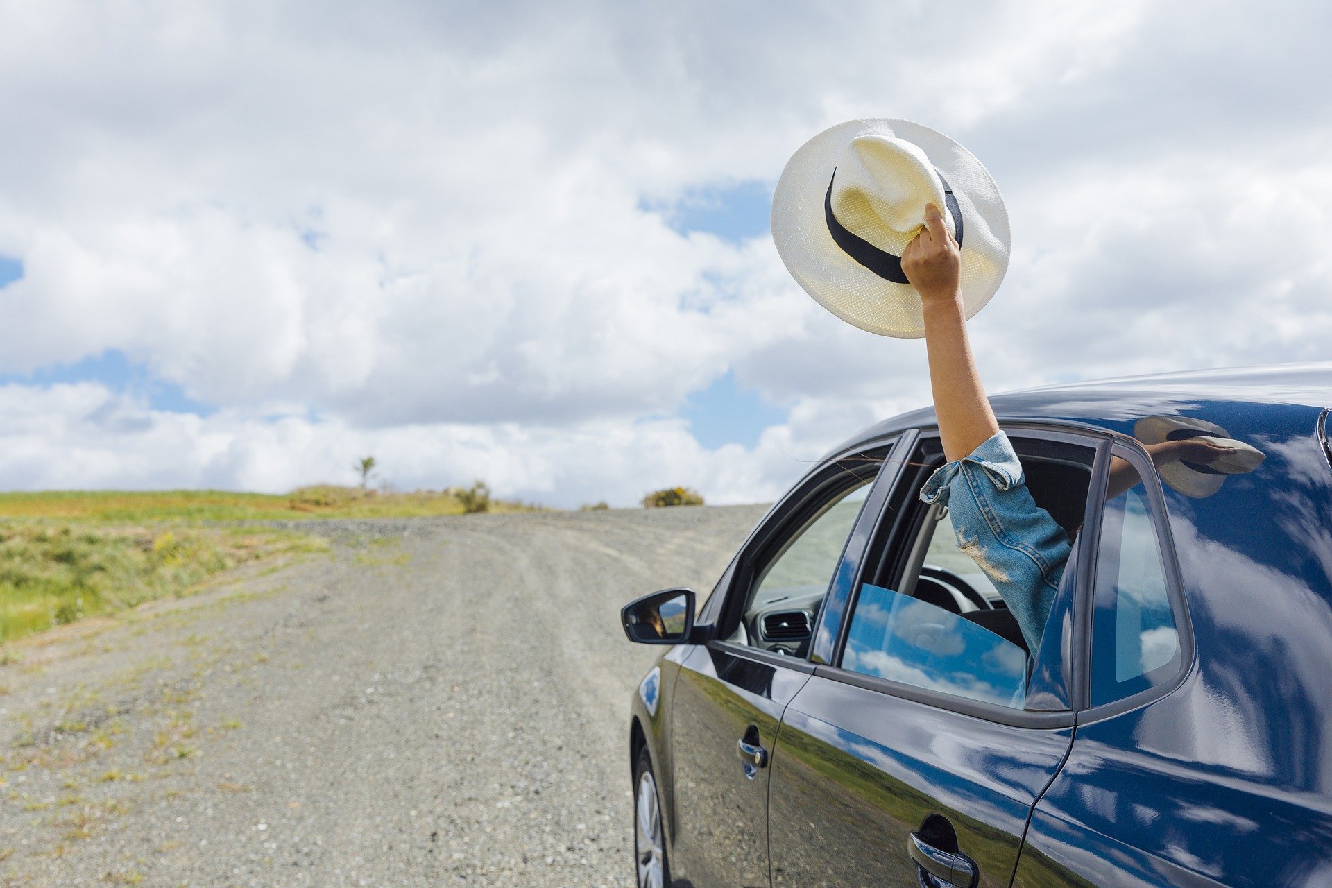 A person holding a hat out the window of a car