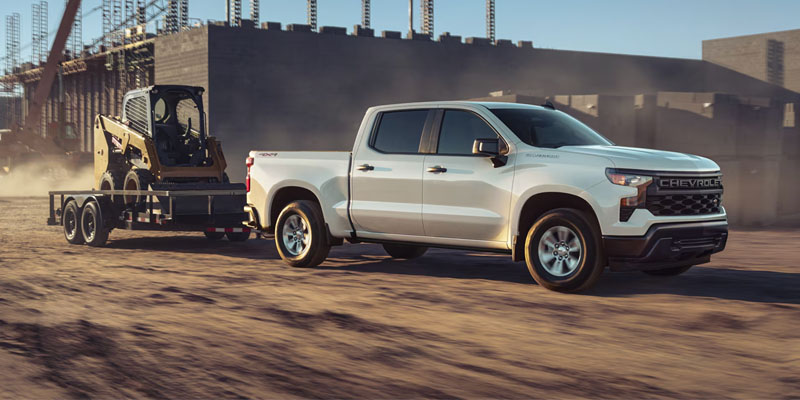 White Chevrolet Silverado towing equipment trailer at construction site.